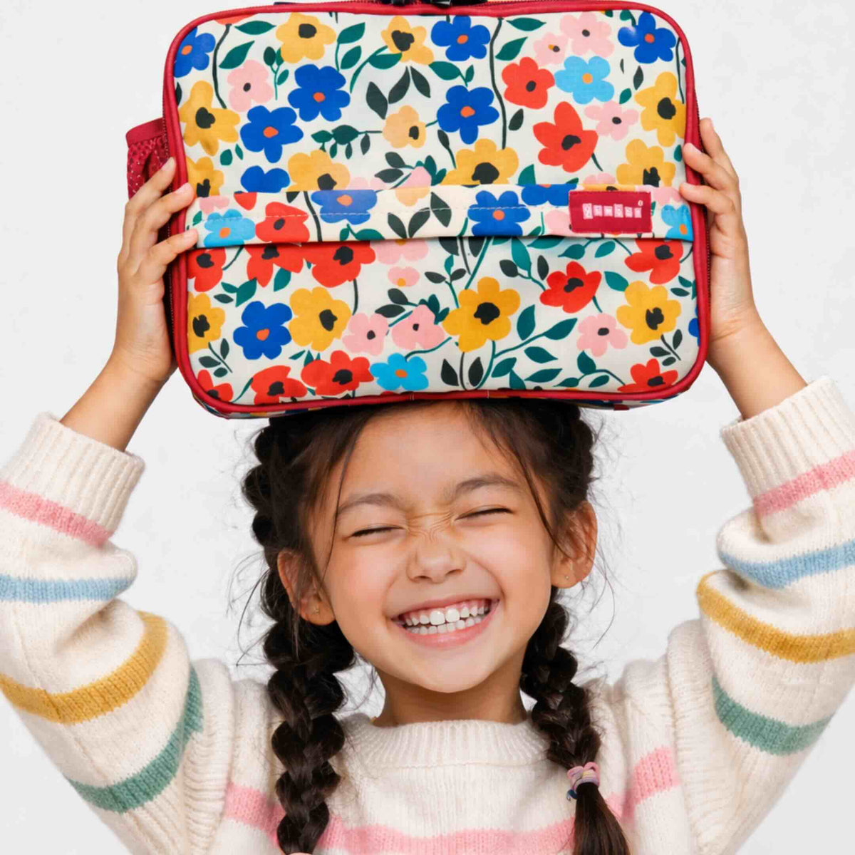 Child holding Yumbox floral-patterned lunch bag above their head with a white background