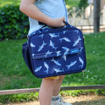 Child holding Yumbox navy blue bag with shark pattern outdoors
